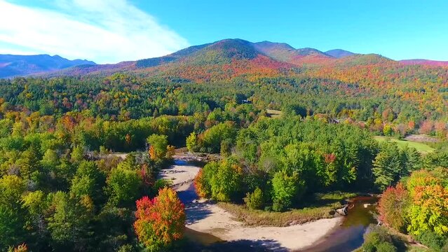 Aerial towards river winding through lush green and fall forest mountains in New York