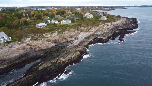 Aerial pan across rocky cliffs and houses on islands of Maine coast during dusk