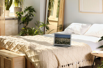 Stylish room interior with comfortable bed, houseplants and modern laptop
