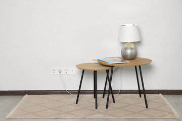 Lamp with magazines on wooden table near white wall, space for text