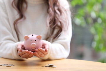 Woman holding piggy bank at table, closeup