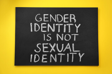 Blackboard with text Gender Identity Is Not Sexual Identity on yellow background, top view