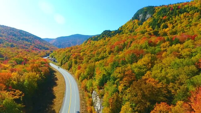 Aerial backwards over stunning road through New Hampshire mountains during peak fall foliage
