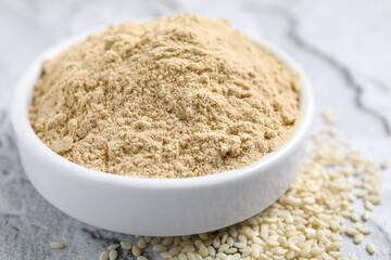Sesame flour in ceramic bowl on white textured table, closeup