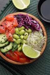 Delicious poke bowl with vegetables, fish and edamame beans on table, flat lay