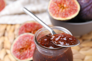 Tasty sweet fig jam with spoon and fruits on table, closeup