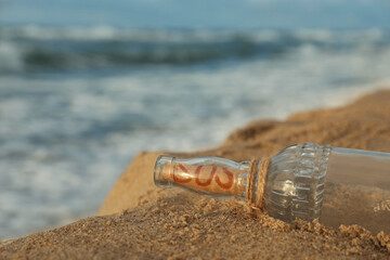 Glass bottle with SOS message on sand near sea, space for text