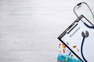 Clipboard with word Rheumatism, stethoscope and pills on white wooden table, flat lay. Space for...