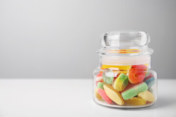 Tasty jelly candies in jar on white table, space for text