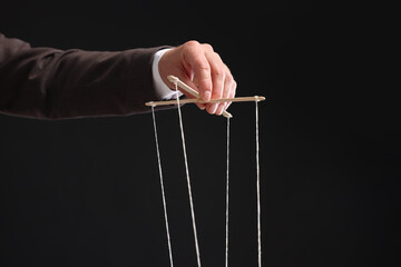 Man pulling strings of puppet on black background, closeup