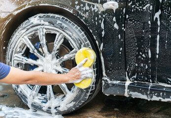 Car service washing car wheels with yellow sponge at outdoor.