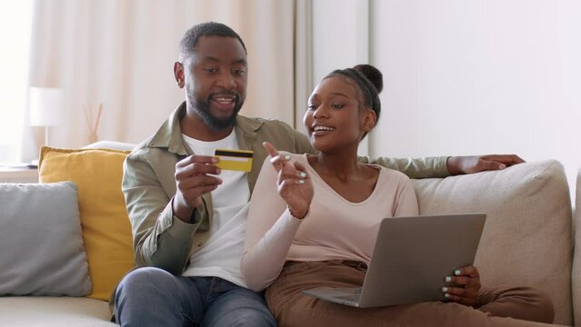Young happy african american couple shopping online together, using credit card and laptop, tracking shot, empty space