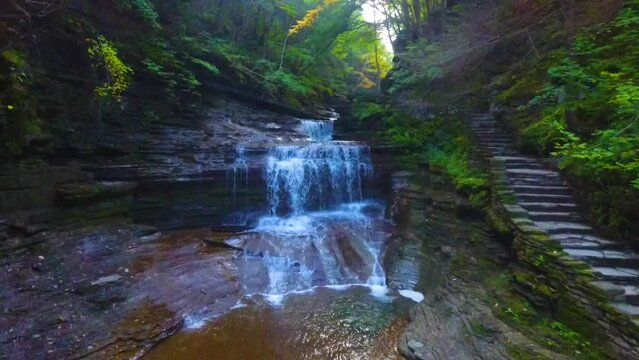 Aerial low through gorge with staircase and waterfall