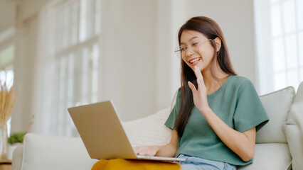 Smiling young asian woman working on laptop at home. Attractive asia female using computer remote...