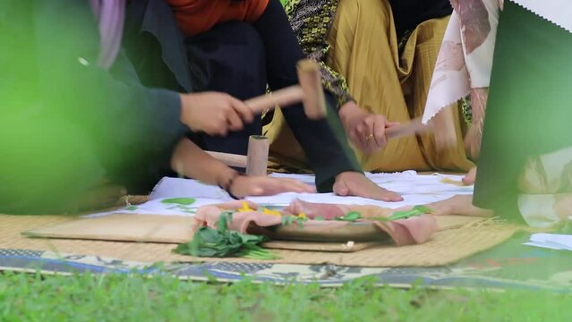 Close-up video, Asian Muslim woman's hands outdoors, making handicrafts, hitting cloth with wooden mallet during ecoprint batik printing process.