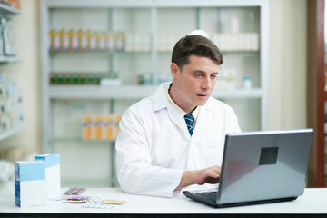 Male pharmacist working in modern pharmacy using laptop.