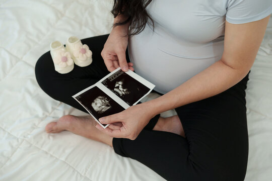 close up pregnant woman looking ultrasound photo of baby with socks or shoes on bed