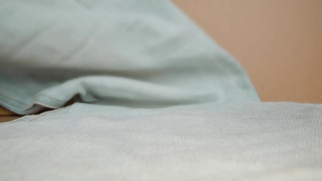 Blue denim pants with yellow stitching lying on table on background of beige colored wall in studio room macro backward motion