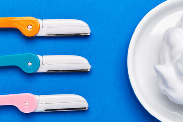 beautiful multicolored razor shavers. Colored razors shavers, on a blue background and shaving foam. copy space for text. view from above.