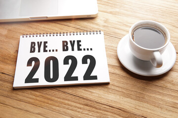 bye bye 2022, words in notebook on table with laptop and cup of coffee.