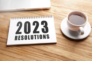 2023 resolution, motivational words in notebook on table with laptop and cup of coffee.