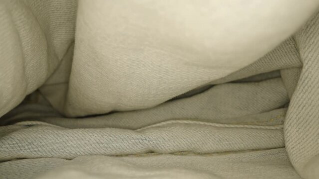 Neatly folded blue and white jeans with yellow stitching and button lying on table on background of studio room macro backward motion