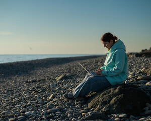 Naklejka na ściany i meble Caucasian woman working freelance on laptop on the beach. 