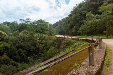 Fototapeta na wymiar Sharp curve of an old inactivated road that connects the cities of Santos and Sao Paulo. Path surrounded by nature and with a rusty guard rail on the sides. part of the State Park Caminhos do Mar