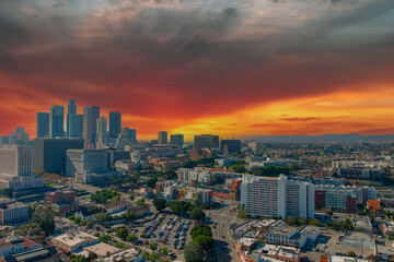Fototapeta na wymiar aerial shot of the skyscrapers, office buildings and apartments in the city skyline with cars driving on the street and lush green trees with powerful clouds at sunset in Los Angeles California USA