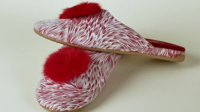 Pair of new women's slippers with a colorful red and white pattern and a scarlet pom-pon. Warm and comfortable female slippers on light background close-up. Toncept of cozy and comfortable home shoes