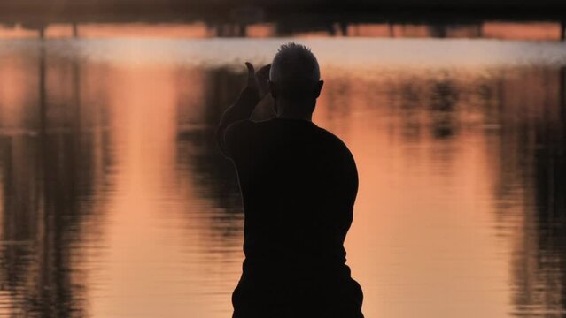 mature healthy man practices taichi moving meditation in the nature by the lake,body mind relaxation activity