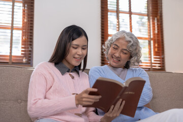 Asian mother and daughter spent the holidays in the living room showing their love for each other by reading to their mother at home happily and warmly.