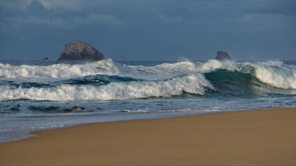 Waves breaking on the beach, with a rocky islet in the background, in the morning in Zipolite, Mexico