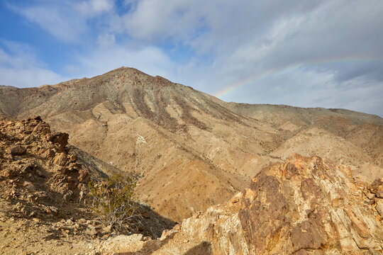Mountains and foothills with a subtle rainbow in a blue sky with clouds near Palm Springs California USA