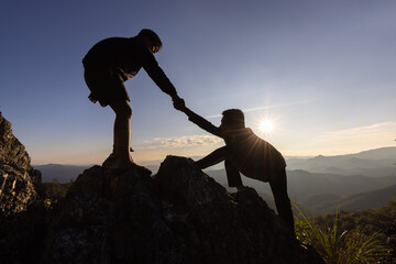 Silhouette of helping hand between two climber.  couple hiking help each other silhouette in mountains with sunlight. The men helping pull people up from high cliffs