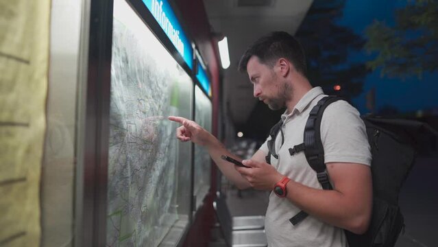 Male passenger analyzes transport card at a public transportation stop and matches it to an app on his phone in Munich, Germany. Checking map and waiting for transport in city. Public transport route