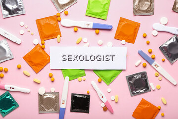 Paper with word SEXOLOGIST, pills, condoms and pregnancy test on pink background