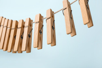 Many wooden clothespins hanging on rope against blue background, closeup