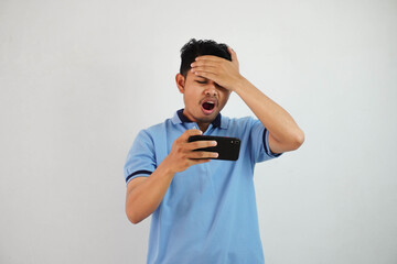 young asian man the effect of being disappointed when you lose playing a game online with smartphone and holding your forehead isolated on white background