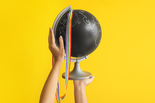Female hands with globe and LGBT ribbon on yellow background