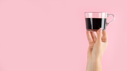 Arms raised up holding coffee cup on pink background.