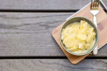 Bowl with creamy potato salad and fork on tray against grey wooden background