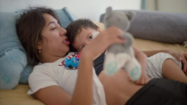 Brunette latin mother breastfeeding her baby boy on a bed with light brown sheets after waking up on a warm morning