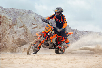 Young man practice riding dirt motorcycle. Splashing sand