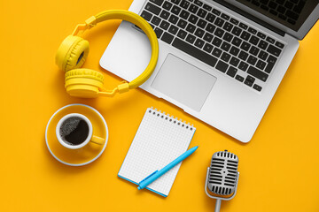Notebook with coffee cup, microphone, headphones and laptop on orange background. Podcast concept