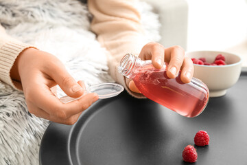Woman pouring syrup for sore throat into spoon at home, closeup