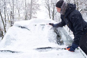 Fototapeta na wymiar Man cleans his car after a snowfall. Cleaning snow from windshield, Scraping ice, Winter car window cleaning