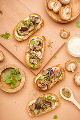 Tasty toasts with mushrooms and bowl of sauce on beige background