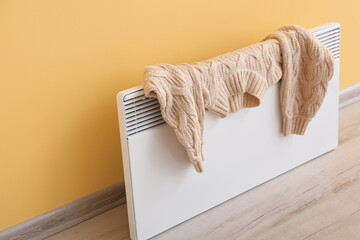 Warm sweater drying on electric radiator near yellow wall