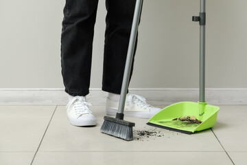 Woman sweeping tile floor with dustpan and broom - obrazy, fototapety, plakaty